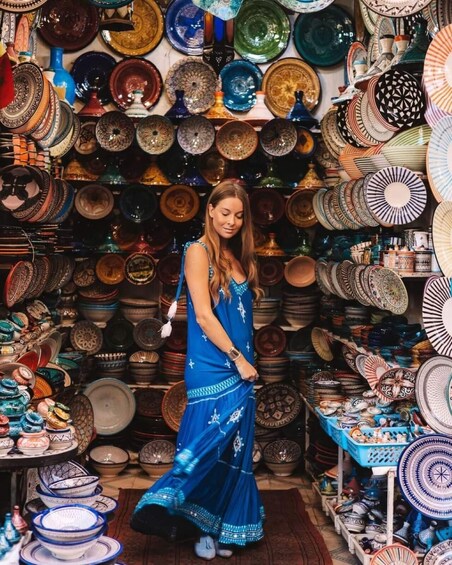 A woman in a blue dress surrounded by a variety of colorful plates and bowls. 1