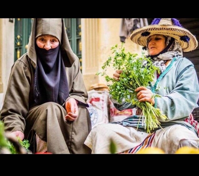 Two individuals seated, one holding a bunch of green plants. 2