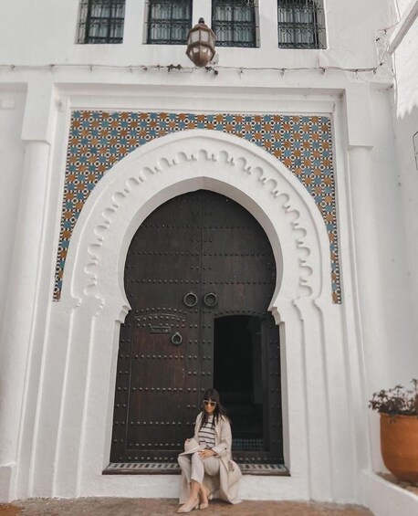 A woman sitting in front of a large, ornate door with a tiled archway. 3