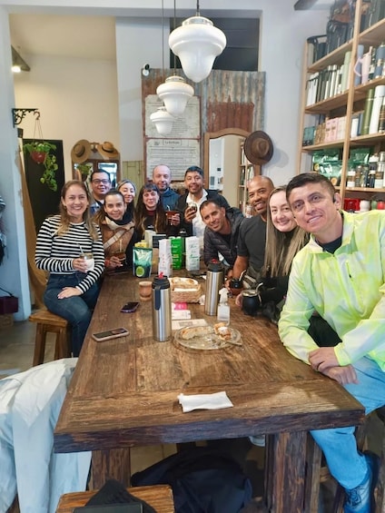 A group of people sitting around a wooden table with various items like bottles and a plate of food. 2