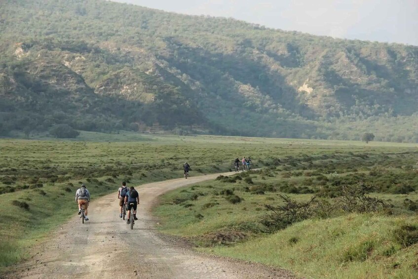 Cyclists on a dirt road in a grassy field with a hilly landscape in the background. 2
