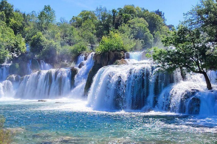 A waterfall cascading over rocks into a clear blue pool surrounded by lush greenery. 1