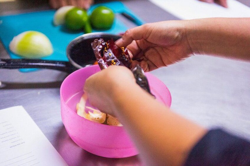 A person holding a spoon with food, a pink bowl, and green vegetables on a cutting board. 5