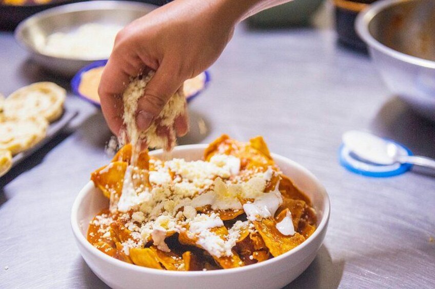 A bowl of nachos topped with cheese and sauce. 1
