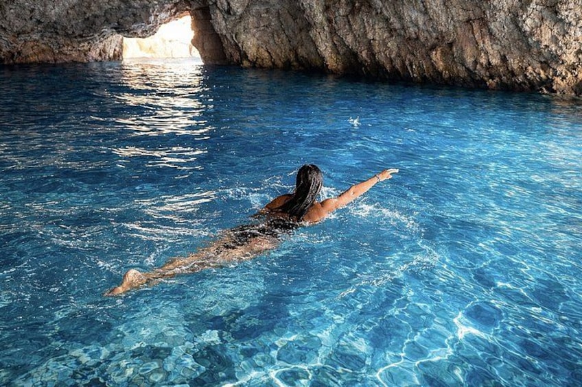 A person swimming in a clear blue pool with a rocky cave entrance in the background. 1