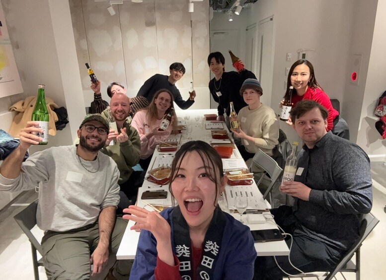 A group of people sitting around a table with food and drinks, in a room with white walls and a concrete floor. 1