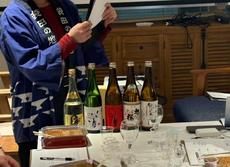 A person in a blue and red jacket holding a menu at a table with various bottles and glasses. 4