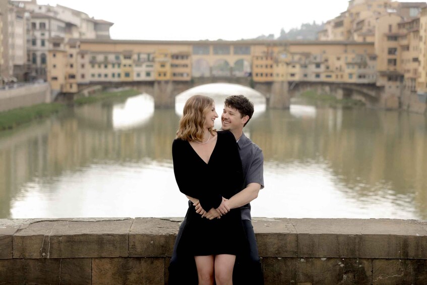 A couple embracing on a bridge with a river and buildings in the background. 2