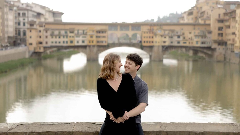 A couple embracing in front of a river with buildings in the background. 2