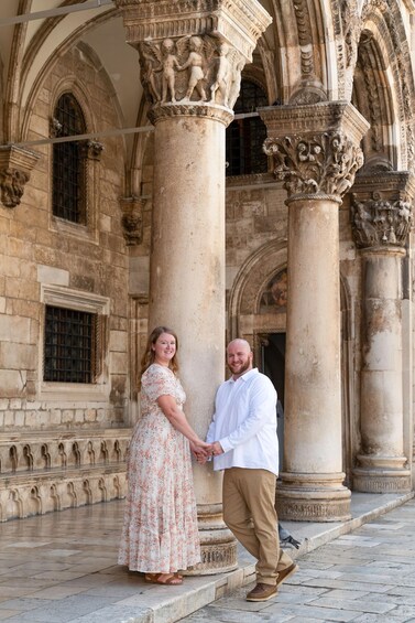 A couple holding hands in front of a historic building with ornate columns and arches. 4