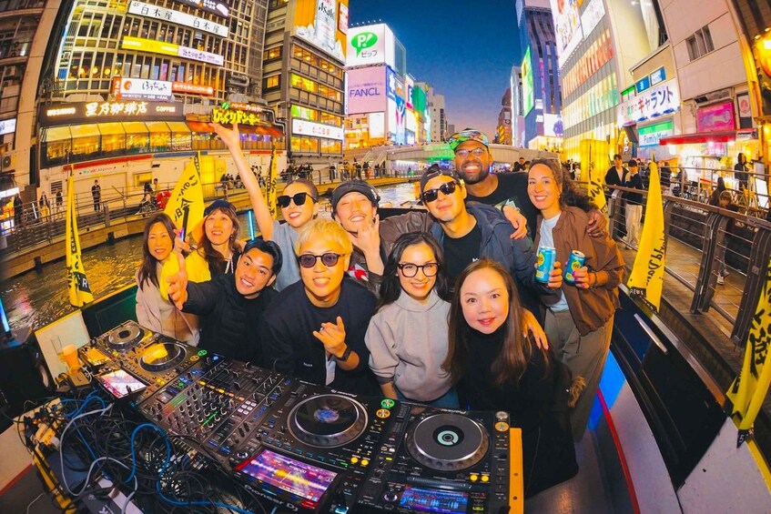 A group of people in a city street with illuminated buildings and a DJ booth. 3
