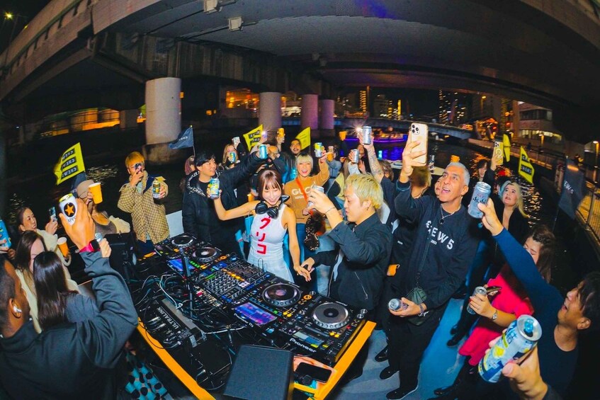 A group of people gathered around a DJ booth, holding up phones and cans, in an urban setting with buildings in the background. 4