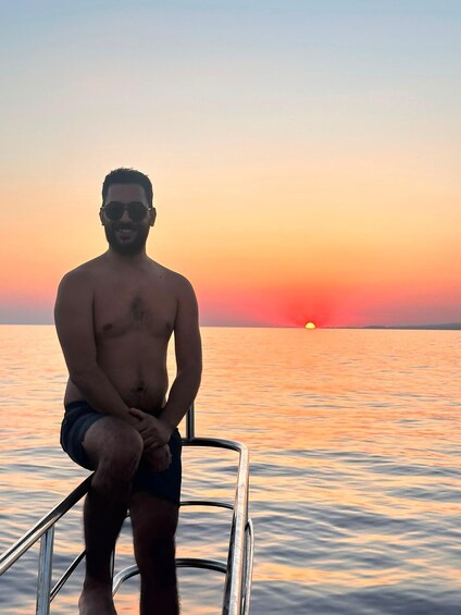 A person sitting on a boat railing during sunset. 2