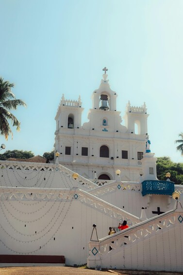 A white church with a bell tower and a cross on top, surrounded by palm trees. 3
