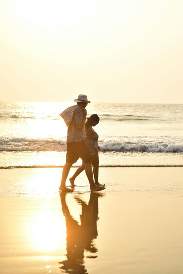 A couple walking on a beach at sunset with ocean waves in the background. 5