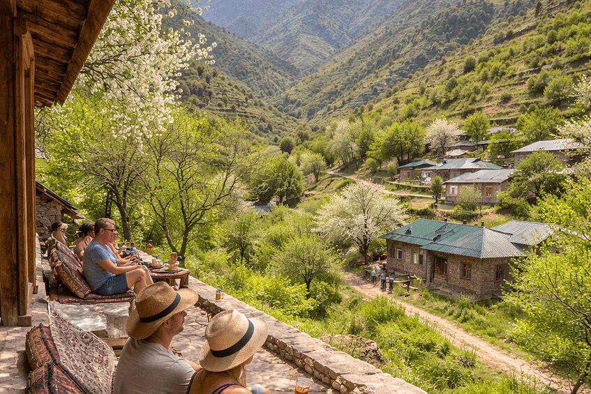 A mountainous landscape with a stone building and a few people sitting on a terrace. 4