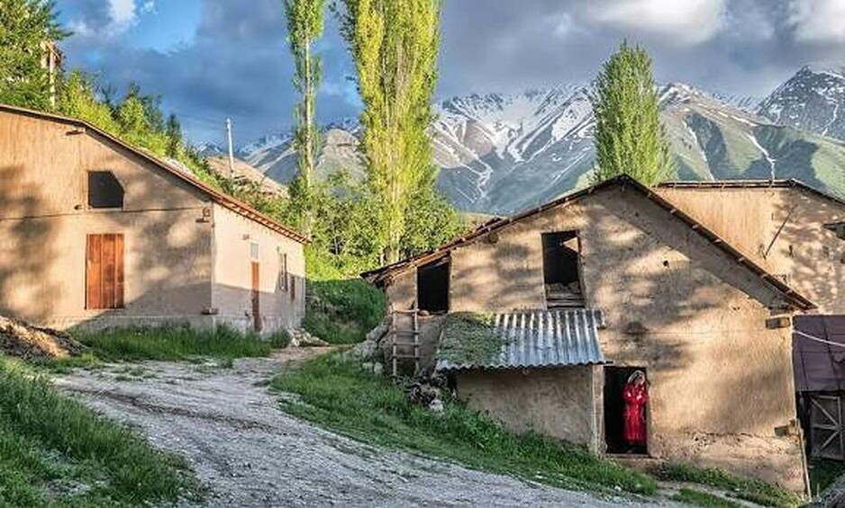 A rural road with two rustic buildings, a mountain range in the background, and a clear sky. 1