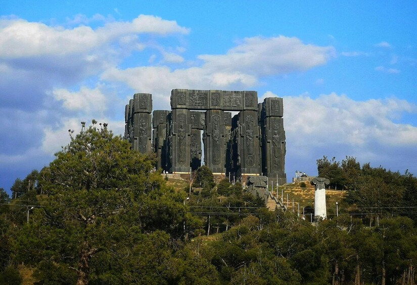A large stone monument with intricate carvings, surrounded by trees and a clear sky. 5