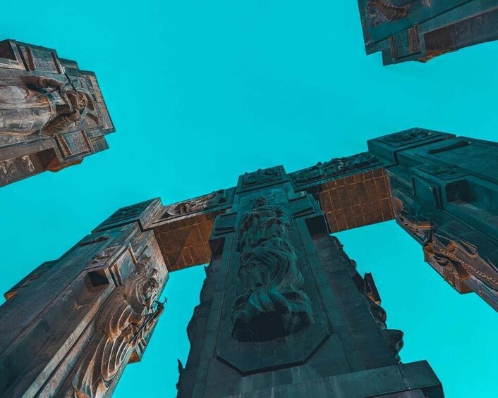 A tall, intricately carved stone structure with a central figure, viewed from below against a clear blue sky. 3