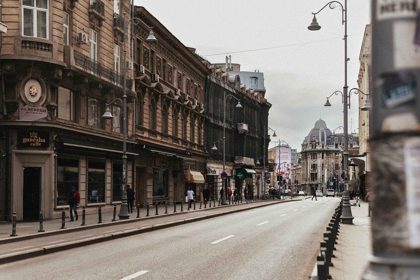A street with buildings, a domed structure, and pedestrians. 5