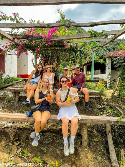 Un grupo de personas sentadas en bancos de madera en un jardín con flores rosadas y follaje. 3