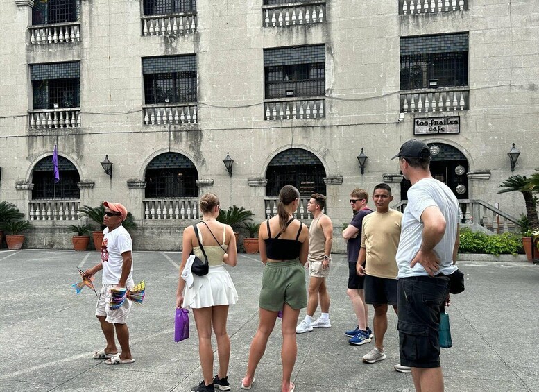 A group of people standing in front of a historic building with arched windows and a sign that reads "Los Frailes Cafe". 4