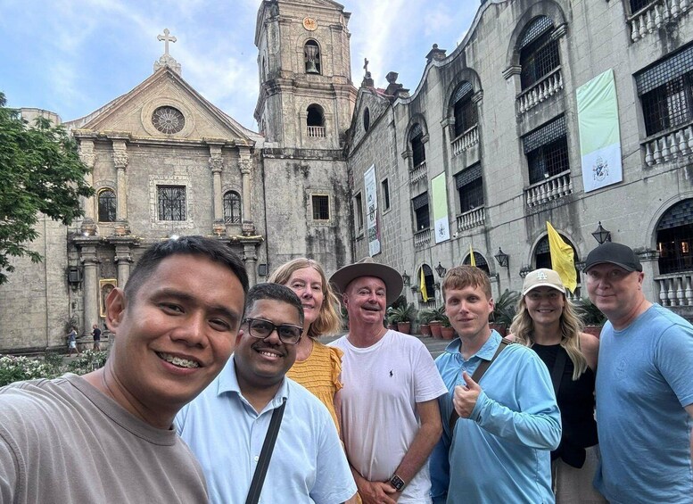 A group of people posing in front of a historic church with a bell tower and a large clock. 1