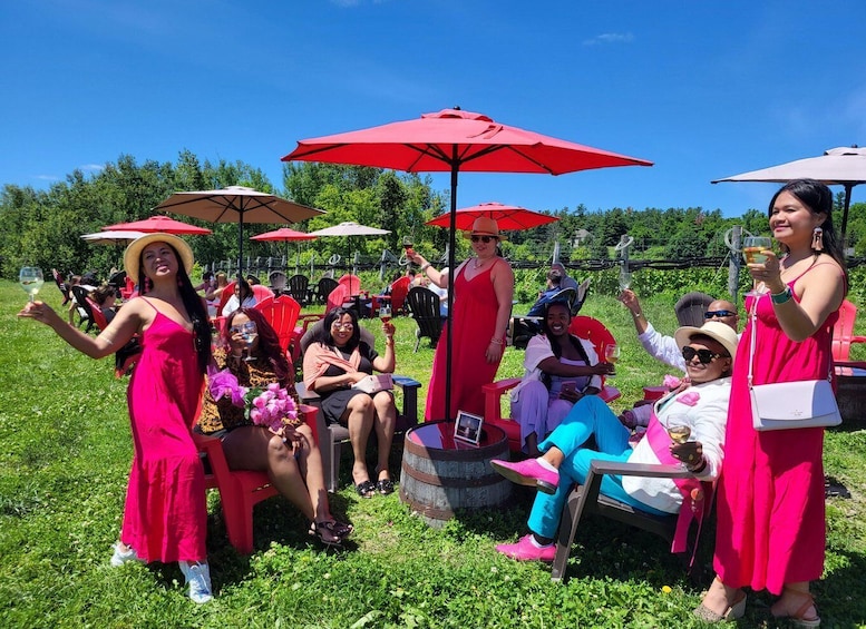 People sitting and standing under red umbrellas in a grassy outdoor setting. 1
