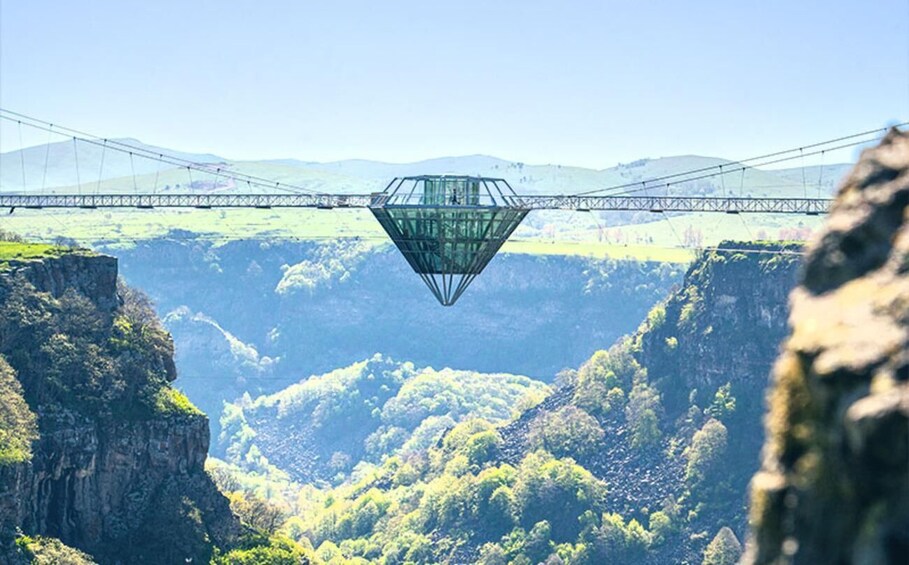 Una gran estructura en forma de diamante suspendida sobre un valle, con un puente al fondo. 1