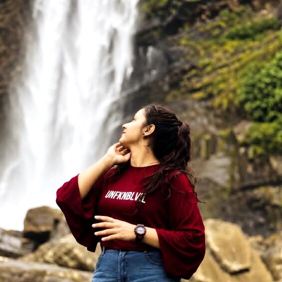 A person standing in front of a waterfall with a red shirt and jeans. 3