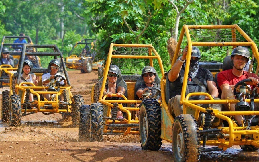People driving off-road vehicles on a dirt path surrounded by greenery. 1