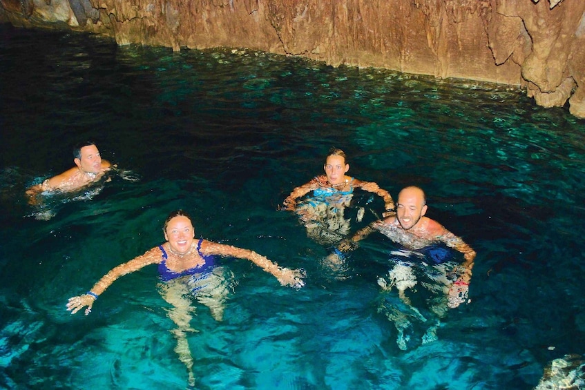 People swimming in a clear blue pool with rocky walls. 4