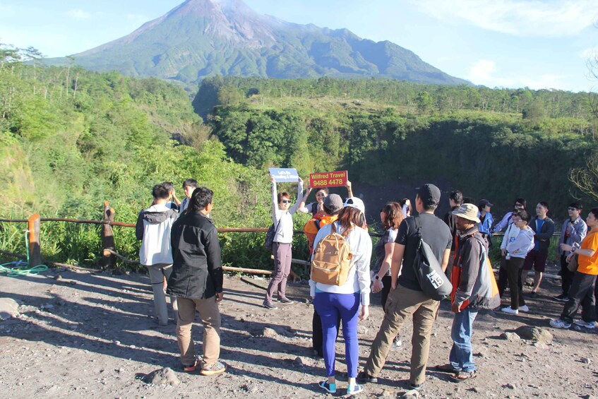 A group of people standing on a dirt path with a volcano in the background. 5