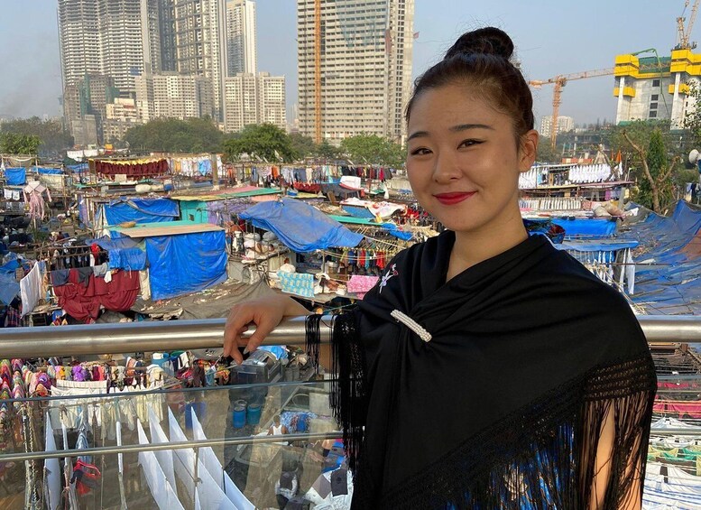 A woman standing on a balcony overlooking a crowded market with makeshift stalls and buildings in the background. 4