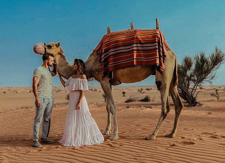 A camel in a desert with a saddle, a person in a white dress, and another person in casual clothing. 4