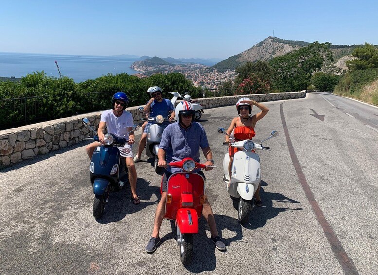 A group of people on scooters on a road with a scenic view of the sea and hills in the background. 2