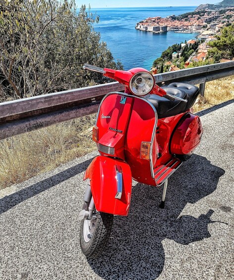 A red Vespa scooter parked on a road with a coastal town in the background. 3