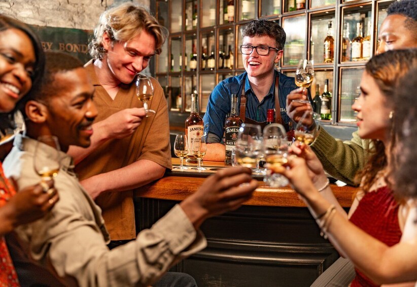 A group of people toasting with wine glasses at a bar with a variety of bottles in the background. 1