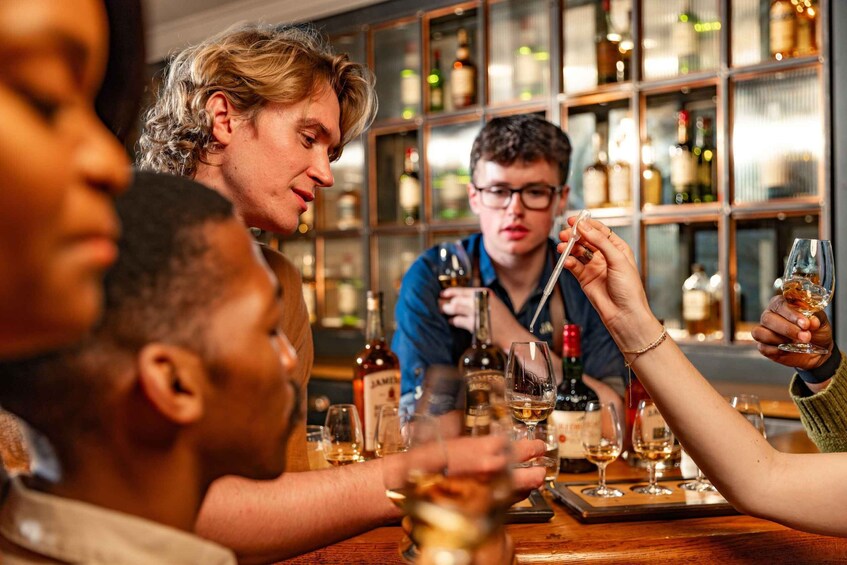 People tasting different types of alcohol at a bar with shelves of bottles in the background. 4