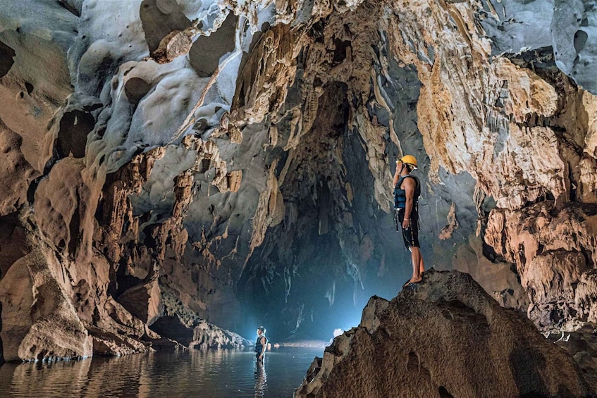 A person standing on a rock inside a cave with water at the bottom. 2