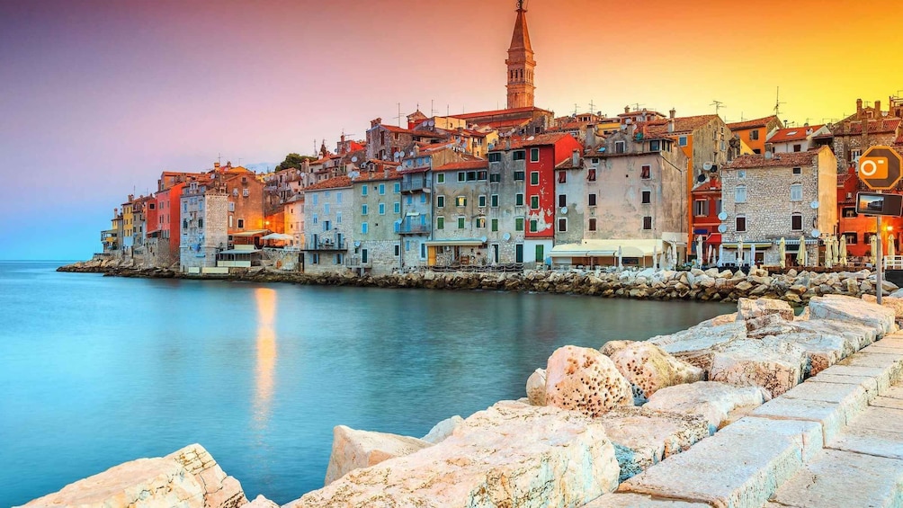 A coastal town with colorful buildings, a prominent tower, and a calm sea. 1