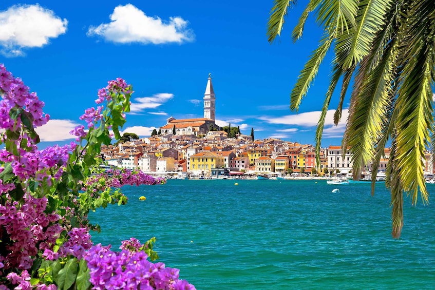 A coastal town with a prominent church tower, colorful buildings, and a clear blue sea. 3