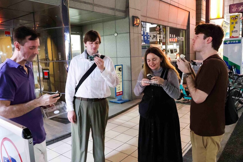 Four people standing outdoors, some eating food. 2