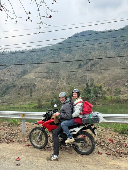 Two people on a motorcycle, with a hilly landscape and a body of water in the background. 3