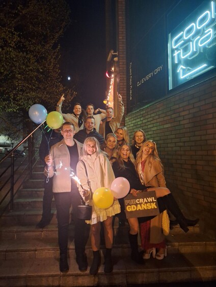 A group of people on stairs at night with a neon sign in the background. 1