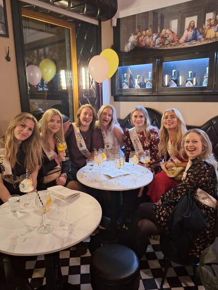 A group of people at a social gathering with a table set for drinks and a painting on the wall. 5
