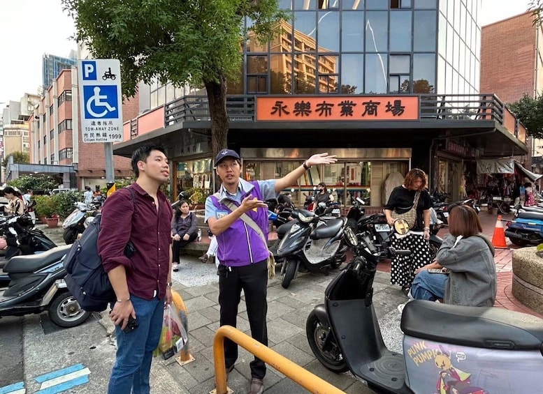 A busy street with people and scooters, a tow-away zone sign, and a building with a sign in a foreign language. 1