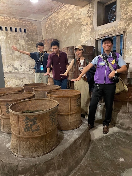 A group of people in a rustic setting with large wooden barrels and a textured wall. 3