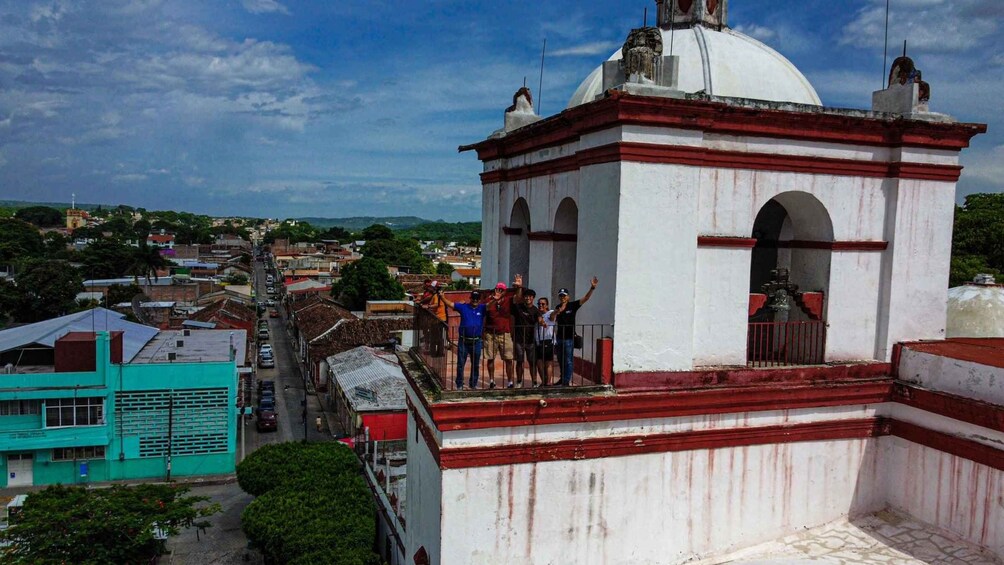 A group of people standing on a white building with red trim, overlooking a cityscape. 1