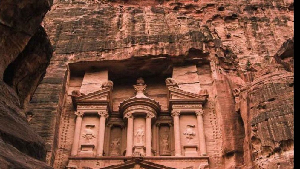 A carved facade with columns and a central statue, set against a rocky cliff. 3